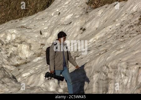 an Indian young man walking through the snow a big camera in hand Stock Photo