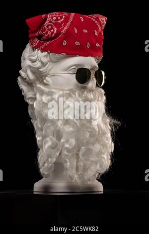 White plaster statue of a bust of Apollo Belvedere with a long white beard in sunglasses and a red bandana shawl on his head Stock Photo