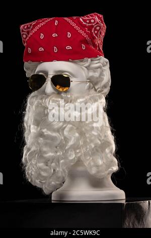 White plaster statue of a bust of Apollo Belvedere with a long white beard in sunglasses and a red bandana shawl on his head Stock Photo