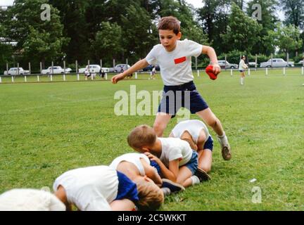School children at school sports day in a park with young boy holding bean bag jumping over other children in a race, International School, Hamburg, Germany in the 1960s Stock Photo