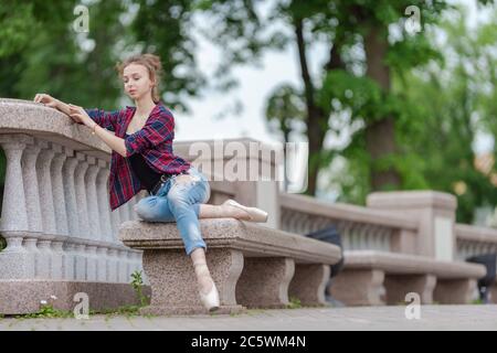 Girl ballerina in jeans, a plaid shirt and pointe shoes dancing in the city on the street Stock Photo