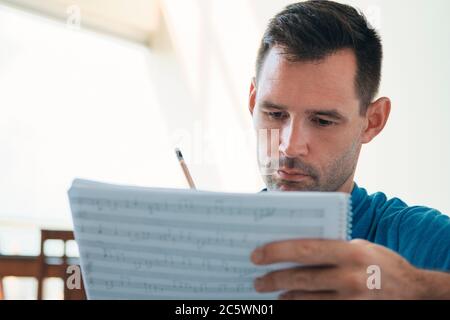 Man Composing Music Using Score Sheets To Write Notes Down Stock Photo