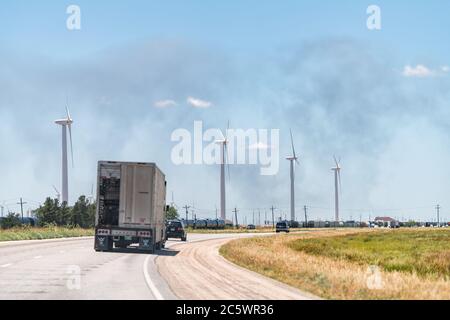 Sweetwater, USA - June 7, 2019: Interstate highway road i20 street in Texas countryside with truck and smoke fire in distance horizon with wind turbin Stock Photo