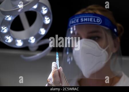 A nurse, wearing a face covering, prepares a syringe to inject a patient Stock Photo