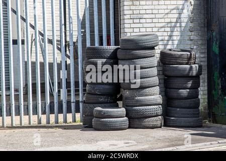 Used car tyres or tires stacked on top of each other outside a car garage or workshop Stock Photo