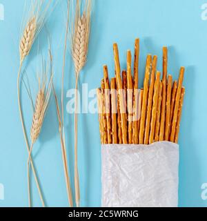 Salted, baked, wheat sticks in a bag made of white ecological paper with wheat spikelets on a blue background Stock Photo