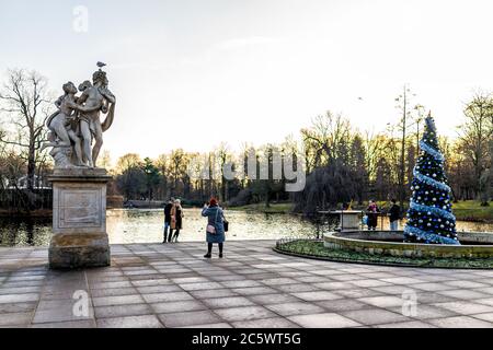 Warsaw, Poland - December 20, 2019: People taking pictures by decorated Christmas tree and canal lake at Warszawa Lazienki or Royal Baths Park Stock Photo