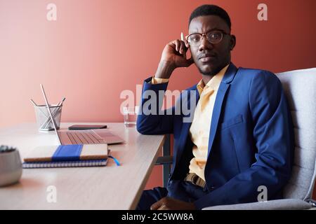 Portrait of young African-American businessman looking away while posing at workplace in office interior against red wall, copy space Stock Photo