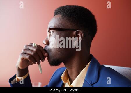 Side view portrait of young African-American businessman thinking while working in office against red wall, copy space Stock Photo