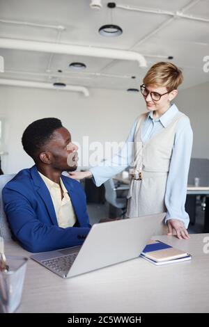 Vertical portrait of smiling female manager talking to African-American colleague standing by him and smiling, copy space Stock Photo