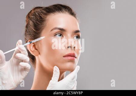 Young beautiful woman getting botox injection over grey background Stock Photo