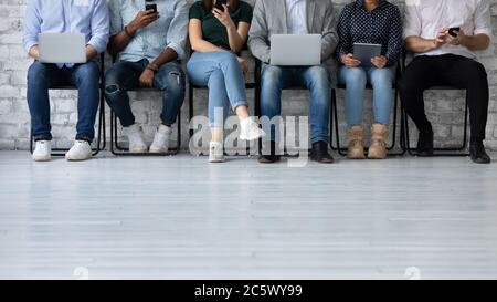 Six multiethnic young people sit in queue holding electronic devices Stock Photo