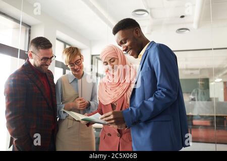 Waist up portrait of contemporary multi-ethnic team discussing business project in office, focus on smiling Muslim businesswoman talking to colleagues Stock Photo