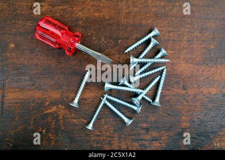 Some many silver screws and small handy screw driver on brown wooden surface top view closeup view Stock Photo