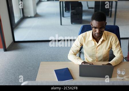 Minimal high angle portrait of elegant African-American businessman using laptop while working at desk in modern office, copy space Stock Photo