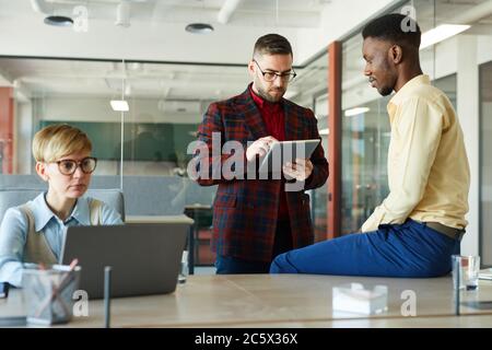Portrait of modern multi-ethnic business team collaborating on work project in conference room, focus on bearded businessman using digital tablet Stock Photo