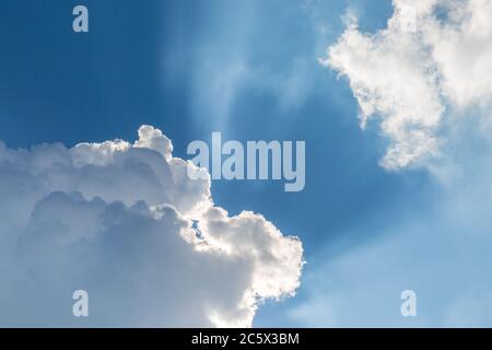 Looking up at sunbeams shining out from fluffy white clouds across a blue sky Stock Photo