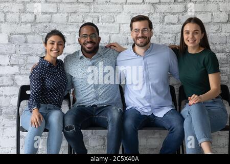 Four multiethnic students friendly office employees embracing seated on chairs Stock Photo
