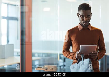 Waist up portrait of young African-American man using digital tablet while standing in doorway at modern office, copy space Stock Photo