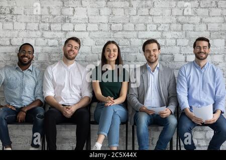 Five multiethnic applicants wait job interview smiling looking at camera Stock Photo