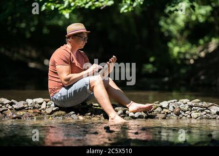Freelance worker working in idyllic environment. Stream in summer in nature. Stock Photo