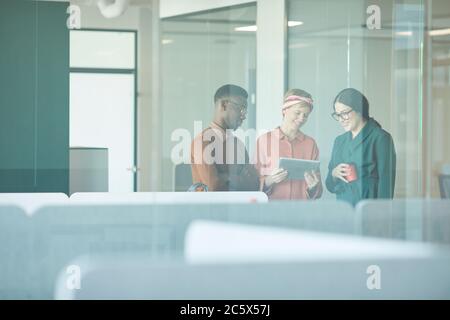 Waist up portrait of three smiling business people discussing work while standing behind glass wall in office, copy space Stock Photo