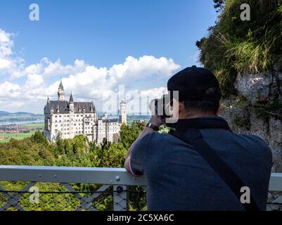 A tourist aims his lens at Neuschwanstein Castle. This 19th-century Romanesque Revival palace perches on a rugged hill above the village of Hohenschwa Stock Photo