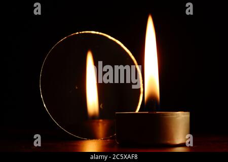 burning candle next to a mirror showing its reflection, dark background Stock Photo