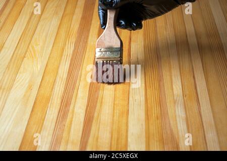 Hand in a black glove paints. Painting with a brush on a wooden table. Treatment of a wooden surface for protection against aging, moisture, dirt. Stock Photo