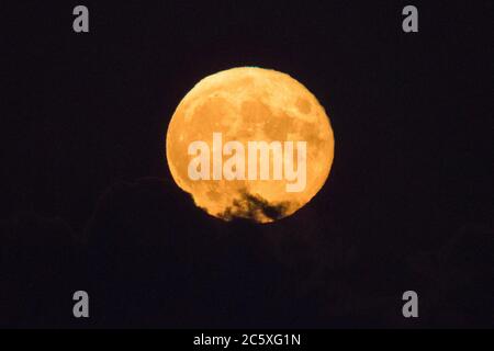 Highcliffe, Dorset, UK.  5th July 2020.  UK Weather. The full Buck Moon glows orange as it emerges from behind a bank of cloud, viewed from Highcliffe in Dorset shortly after moonrise.  Picture Credit: Graham Hunt/Alamy Live News Stock Photo