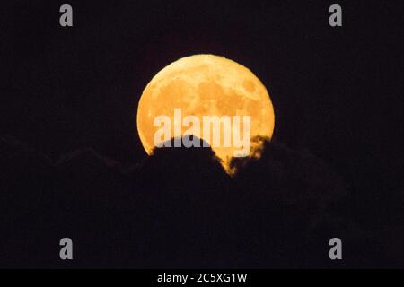 Highcliffe, Dorset, UK.  5th July 2020.  UK Weather. The full Buck Moon glows orange as it emerges from behind a bank of cloud, viewed from Highcliffe in Dorset shortly after moonrise.  Picture Credit: Graham Hunt/Alamy Live News Stock Photo