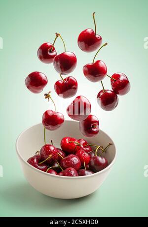 cherries flying on green background, white bowl Stock Photo