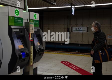 An elderly Japanese man wearing a face mask approachs a Suica vending machine at a platform in Tokyo Station. Tokyo, Japan. Stock Photo