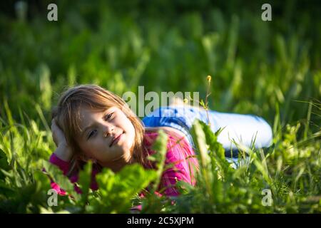 A cute little girl relaxes in the green grass in a meadow. Stock Photo