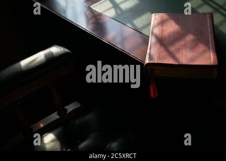 Closed bible on the edge of a red wood and leather table. Copy space. Stock Photo