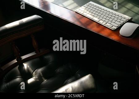 Computer keyboard on wood and leather table. Light play forming lines and shadows. Copy space. Stock Photo