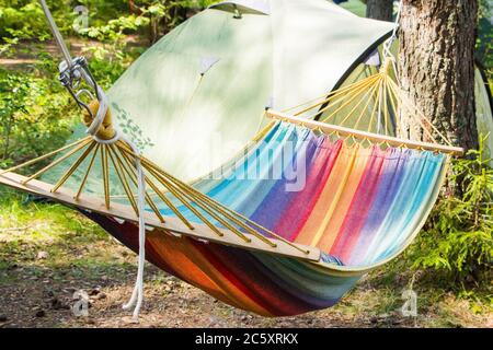 Camping outdoors - tents, equipment and cooking. Camping in the summer. Multi-colored hammock hanging on the trees. Stock Photo