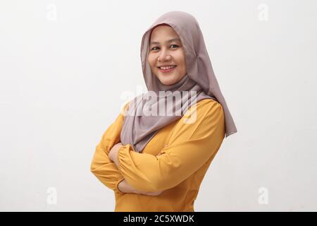 Portrait of Asian muslim woman wearing hijab smiling friendly with crossed arms, confident gesture, successful businesswoman, side view isolated on wh Stock Photo