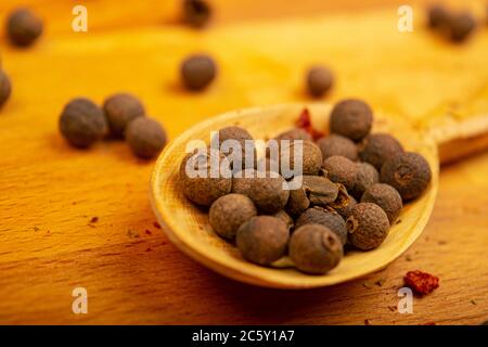 Black allspice peas in a wooden spoon on a wooden background. Close up Stock Photo