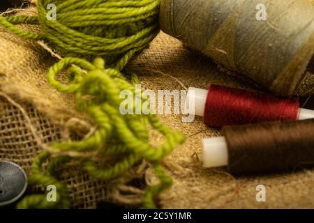 Various buttons and multicolored threads on coarse-textured burlap. Close up Stock Photo