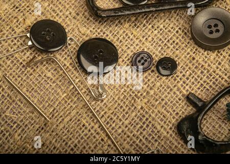 Pins of various sizes, tailor's scissors, and various buttons on coarse-textured burlap. Close up Stock Photo