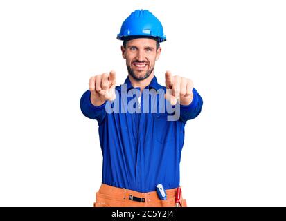 Young handsome man wearing worker uniform and hardhat pointing to you and the camera with fingers, smiling positive and cheerful Stock Photo