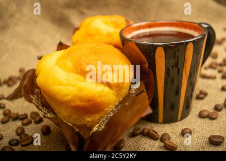 Two fresh cupcakes, a coffee mug, and coffee beans on a rough-textured homespun fabric. Close up Stock Photo