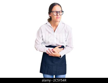 Beautiful brunette young woman wearing professional waitress apron with hand on stomach because indigestion, painful illness feeling unwell. ache conc Stock Photo