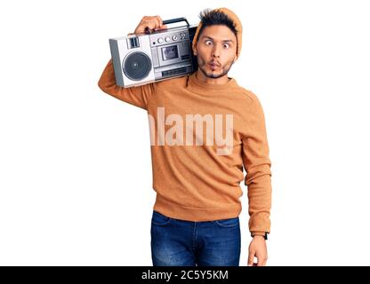 Handsome latin american young man holding boombox, listening to music making fish face with lips, crazy and comical gesture. funny expression. Stock Photo