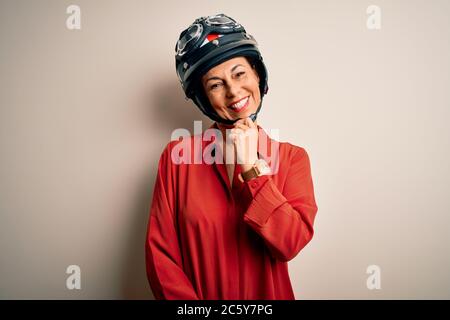 Middle age motorcyclist woman wearing motorcycle helmet over isolated white background looking confident at the camera with smile with crossed arms an Stock Photo