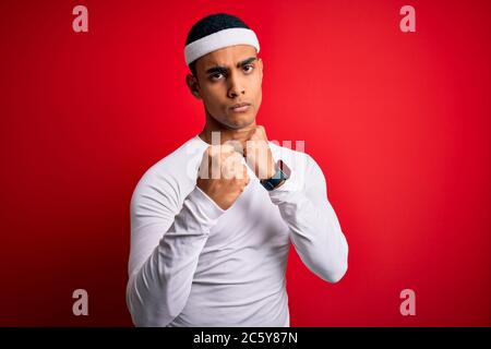 Young handsome african american sportsman wearing sportswear over red background Ready to fight with fist defense gesture, angry and upset face, afrai Stock Photo