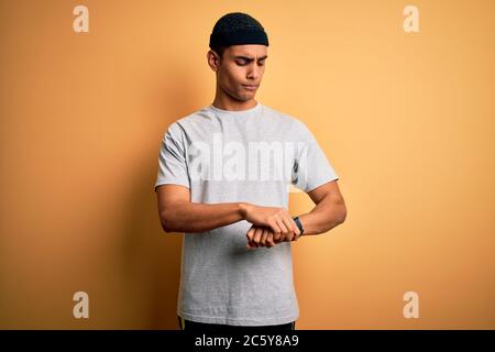 Handsome african american sportsman doing sport wearing sportswear over yellow background Checking the time on wrist watch, relaxed and confident Stock Photo