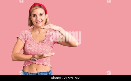 Young blonde woman wearing casual clothes and diadem gesturing with hands showing big and large size sign, measure symbol. smiling looking at the came Stock Photo