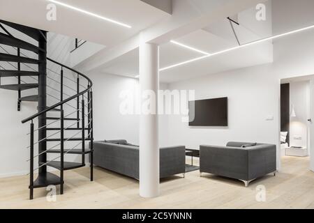 Spacious apartment in white with spiral stairs, pillar, led ceiling lights and simple living room with tv Stock Photo